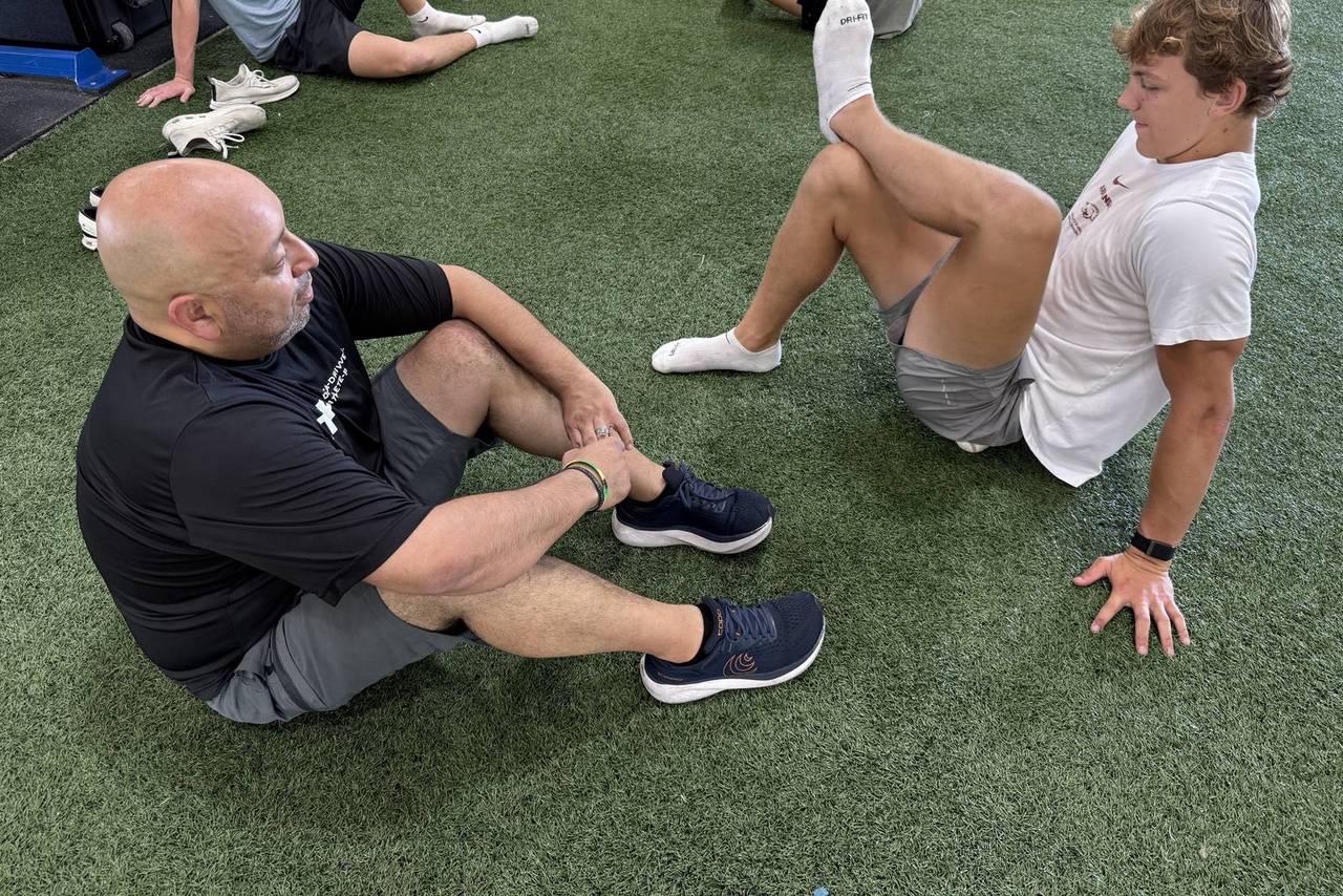 iTOP clinician leading a seated hip mobility drill with an athlete on the turf