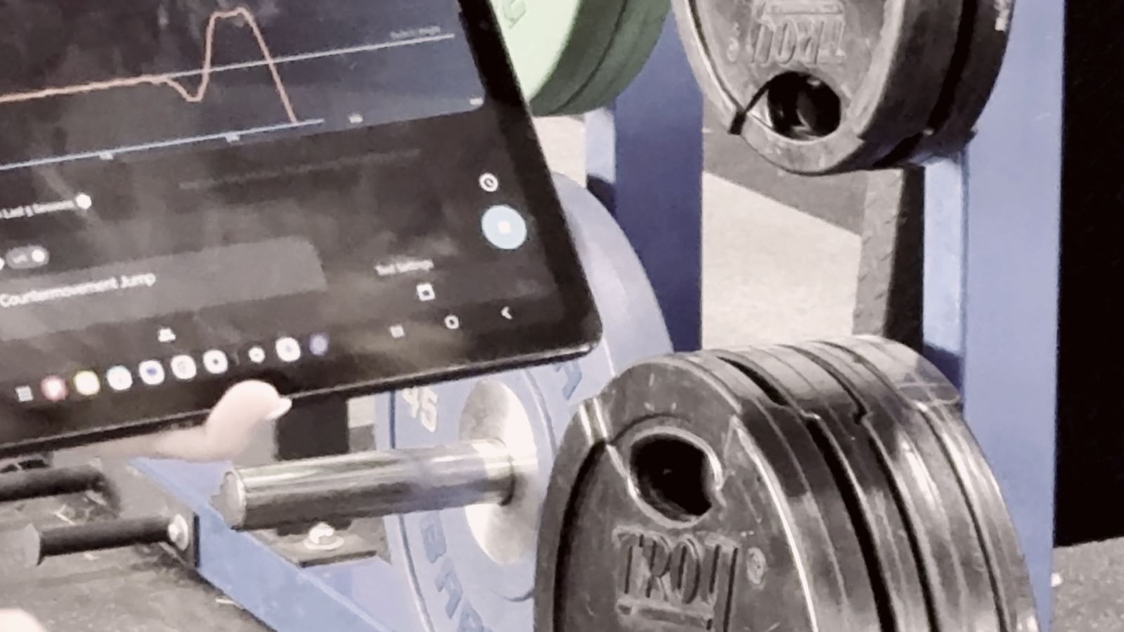 Countermovement jump force trace on a clinician's tablet beside the squat rack