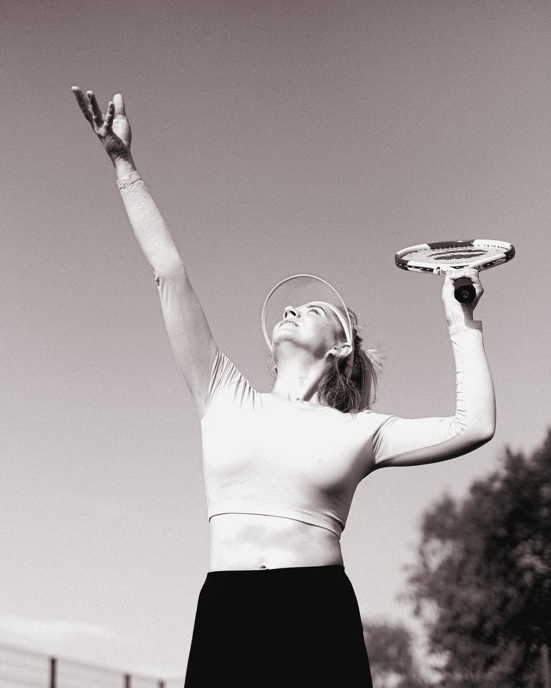 Adult woman reaching overhead to serve a tennis ball