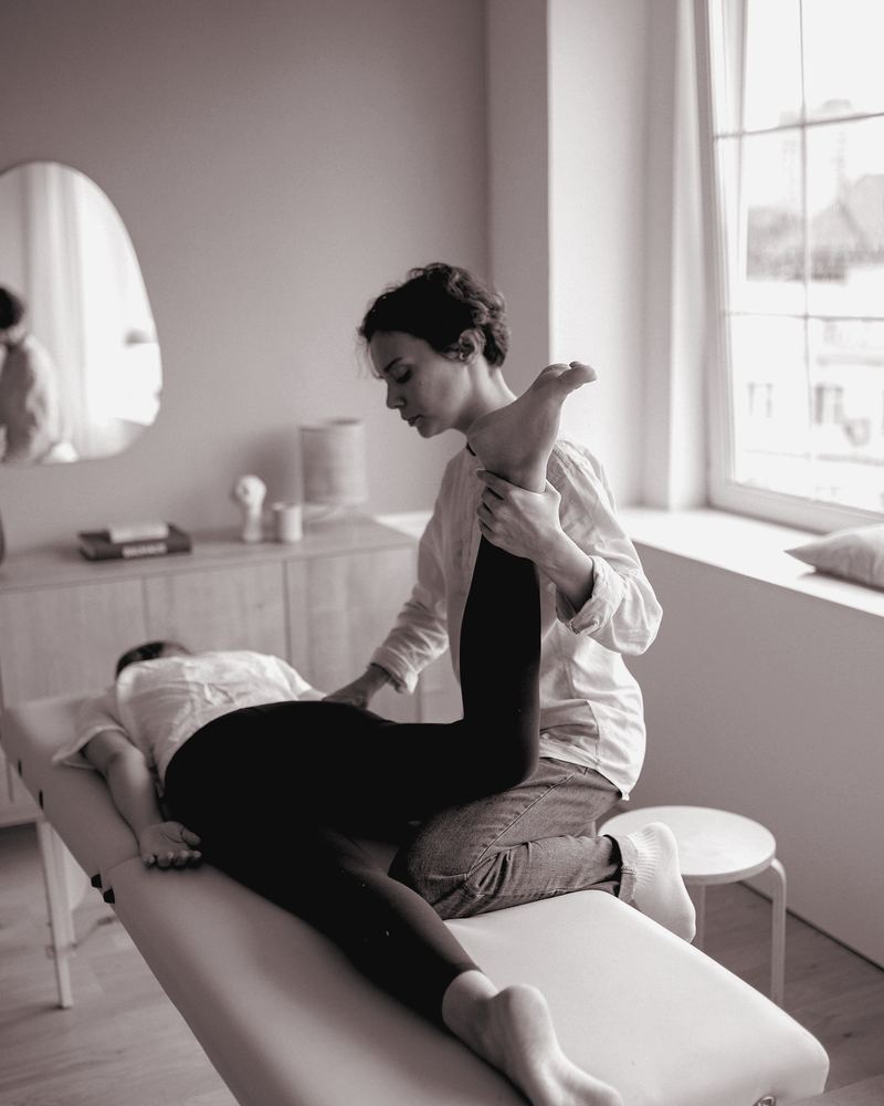 Clinician guiding an adult patient's leg through a stretch on a treatment table