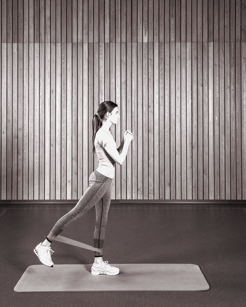 Adult woman doing a resistance-band leg exercise on a mat