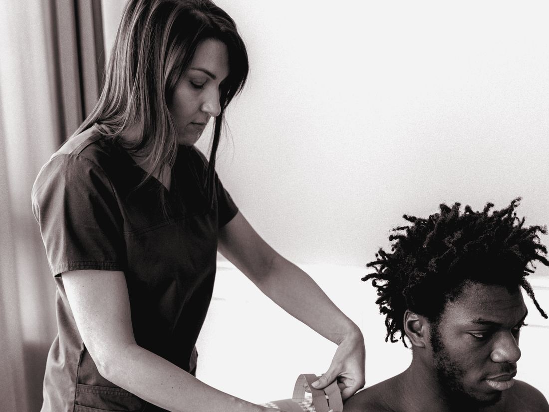 Clinician applying kinesiology tape to an adult athlete's shoulder