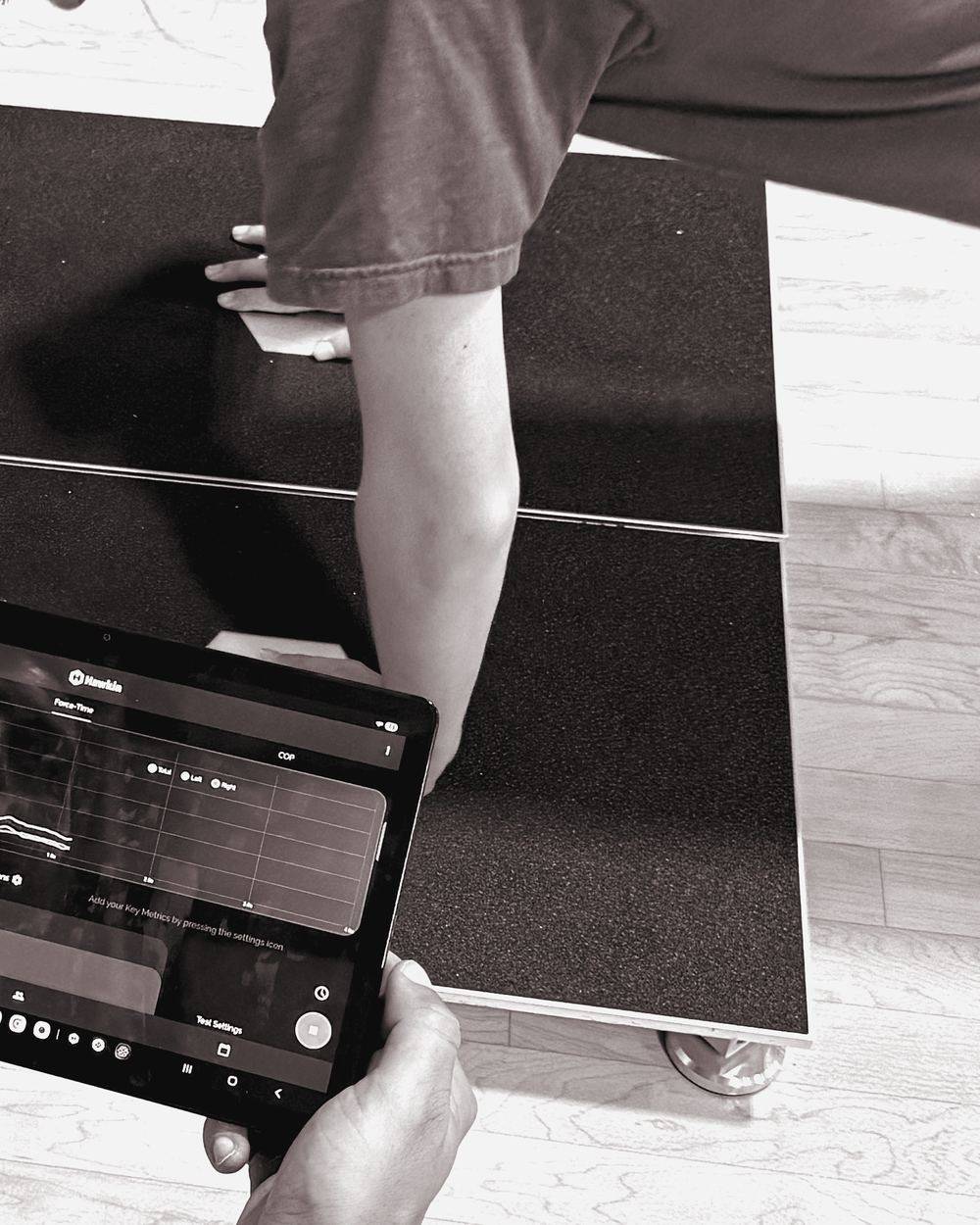 Clinician holding a tablet with a live force trace while an athlete does a push-up on force plates